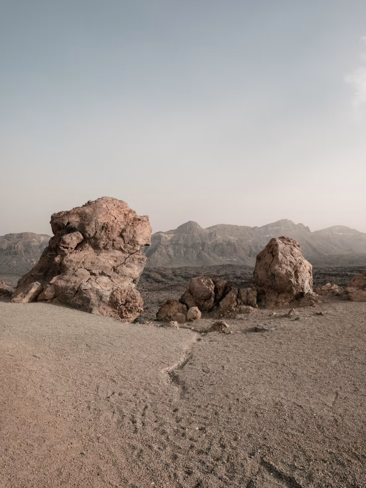 A rocky desert with the backdrop of sandy mountains.