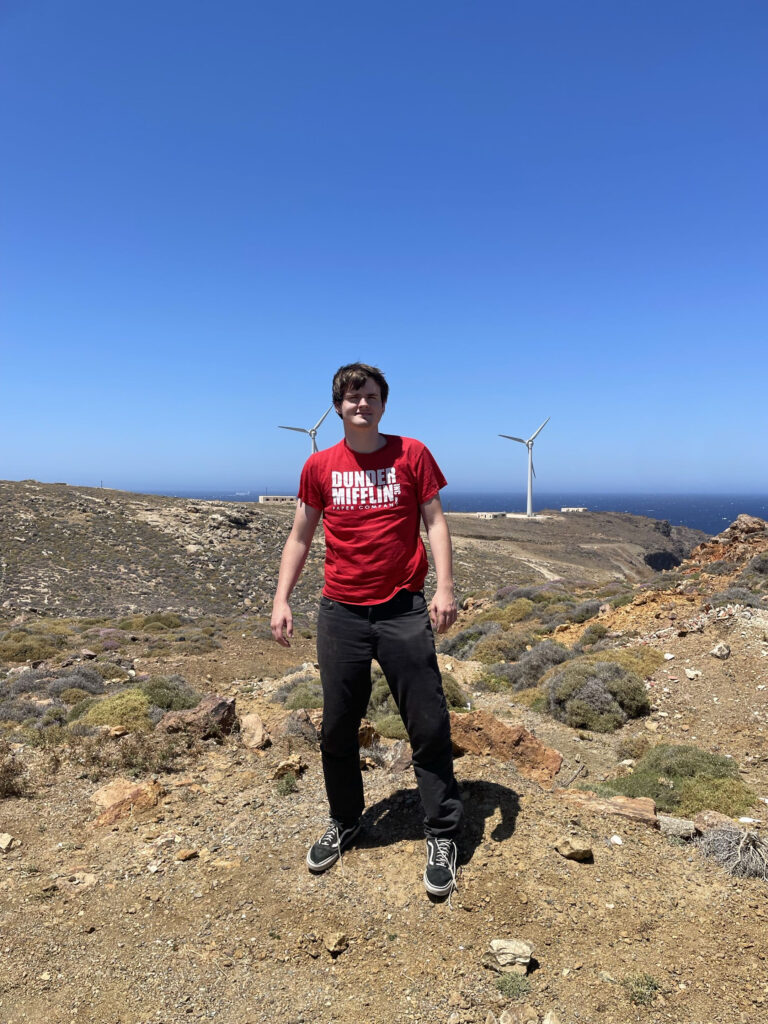 A person standing on a rocky overlook to the ocean with the backdrop of wind turbines.